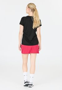 Svart idrottströja med korta ärmar som är tillsammans med en rosa kjol. Vita strumpor och svarta sneakers kompletterar outfiten.