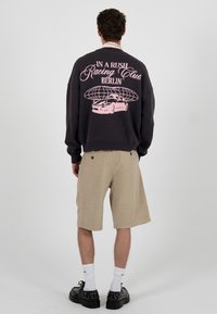 Sweat-shirt gris foncé avec un motif rose représentant une voiture et du texte, associé à un short beige et des chaussures noires épaisses.