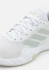 White athletic sneaker with mesh upper, light green Adidas stripes on the side, white laces, and cushioned sole.