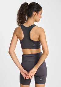 Donkergrijze sportbeha met een racerback ontwerp, gecombineerd met bijpassende high-waisted shorts. Het materiaal lijkt glad en rekbaar, met minimale details.