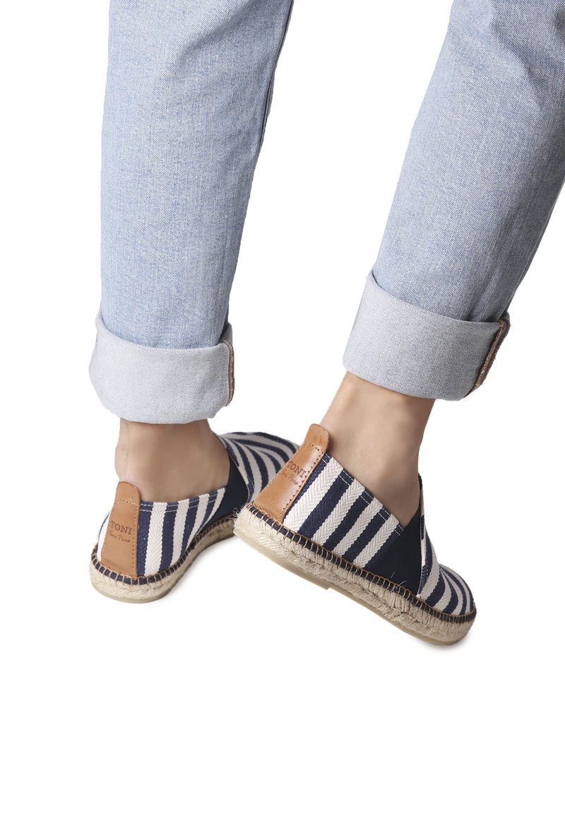Gestreepte instappers van marineblauw en wit stof, met een bruin leren accent en een geweven juten zool. Opvallende lichtblauwe jeans met omslag.