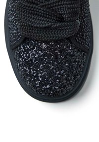 Sneaker nera con una parte superiore testurizzata e luccicante, coperta di piccole paillettes. Presenta lacci rotondi neri e una suola in gomma.
