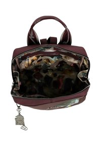 Mochila marrón con un exterior texturizado, apertura con cremallera y un interior con un patrón colorido. Incluye un charm decorativo en el lateral.