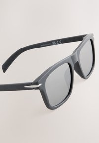 Sive sunčane naočale s mat završetkom, pravokutnim lećama i tankim srebrnim detaljima na krakovima, koje prikazuju moderan dizajn.