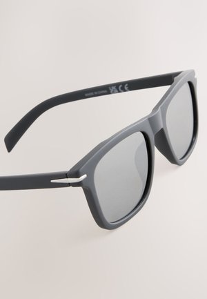 Pilkos saulės akiniai su matinio paviršiaus, stačiakampiais lęšiais ir plonomis sidabrinėmis detalėmis ant kojelių, demonstruojantys modernų dizainą.