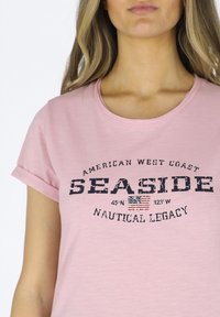 Light pink cotton t-shirt with rolled sleeves, featuring black distressed text reading "SEASIDE" and a small American flag design.