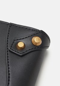 Černá kožená peněženka s pozlaceným kováním, výrazným prošíváním a unikátním šikmým designem se dvěma ozdobnými kovovými nýty.