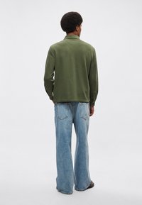 Polo verde a maniche lunghe abbinata a jeans di jeans azzurri a gamba larga, vista posteriore. Tessuto morbido con vestibilità comoda.