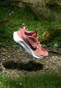 Baskets de course Nike en corail et blanc, présentant une tige texturée, un logo swoosh noir et une semelle légère avec des accents violets.