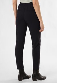 Zwarte op maat gemaakte broeken met een slank model, elastische tailleband, twee achterzakken en een soepele textuur. Gestyled met zwarte enkellaarsjes.