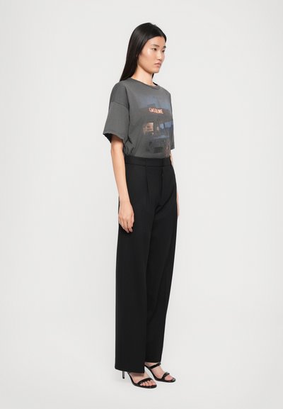 Gray graphic T-shirt with "GASOLINE" text and image, paired with black wide-leg trousers. Model wears black strappy sandals. Smooth textures visible.