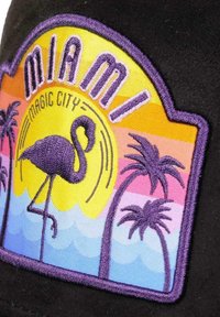 Schwarze Kappe mit gesticktem Patch, der den Text "Miami Magic City", einen rosa Flamingo, Palmen und einen Sonnenuntergangsgradienten im Hintergrund zeigt.