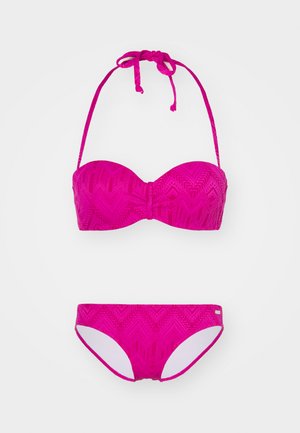 Δίχρωμο μπικίνι σε έντονο ροζ, με υφή σε μοτίβο ζιγκ-ζαγκ. Το τοπ έχει σχέδιο μπαντό και ρυθμιζόμενες τιράντες στο λαιμό, ενώ το κάτω μέρος είναι κλασικής κοπής.