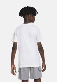 Camiseta de algodón blanca con cuello redondo y mangas cortas, combinada con pantalones cortos grises. La vista posterior muestra una textura suave y un diseño sencillo.