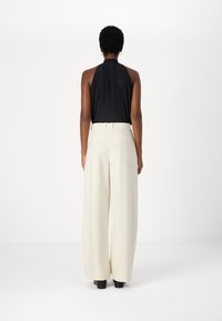 Black pleated sleeveless top with a high neck, paired with flowy, cream wide-leg trousers and black shoes. Simple, elegant design.