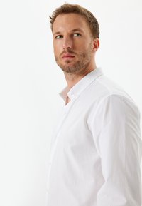 Biała koszula zapinana na guziki wykonana z bawełny. Posiada standardowy kołnierzyk oraz długie rękawy. Miękka struktura z dopasowanym krojem, minimalistyczny design.
