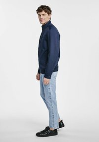 Granatowa kurtka z stójką, bocznymi kieszeniami i ściągaczami na rękawach, zestawiona z jasnoniebieskimi dżinsami i czarnymi sneakersami.