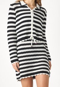 Stickad tvådelad outfit med svarta och vita horisontella ränder, vågiga kanter, knäppbar cardigan och justerbar dragsko i midjan.
