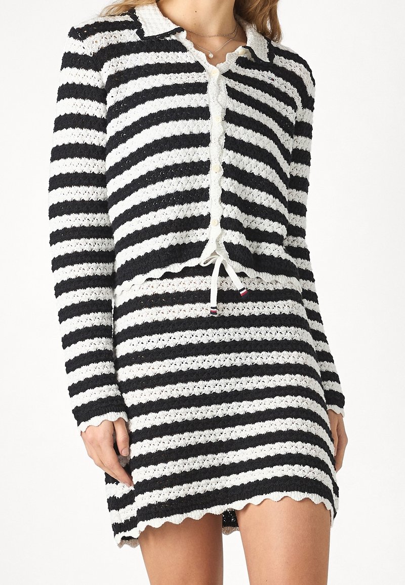 Stickad tvådelad outfit med svarta och vita horisontella ränder, vågiga kanter, knäppbar cardigan och justerbar dragsko i midjan.