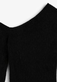 Mustaherkkä vaate, jossa on syvä V-kaula-aukko ja olkapäät paljastava muotoilu, korostaen ryppyistä kangaskuviota.