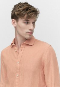 Licht perzikkleurig linnen shirt met een button-down kraag, lange mouwen en geen zichtbare patronen. Beschikt over witte knopen voor sluiting.