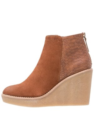 Botte de cheville à talon compensé en suede marron avec un panneau de talon texturé à motif serpent et fermeture éclair sur le côté, dotée d'une semelle plateforme beige légèrement translucide.