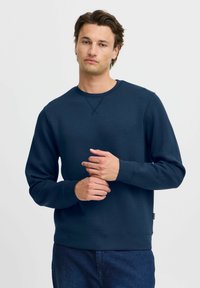 Tengerészkék crewneck pulóver puha anyagból, hosszú ujjal, bordás mandzsettával és laza fazonnal. Minimalista dizájn, minta nélkül.