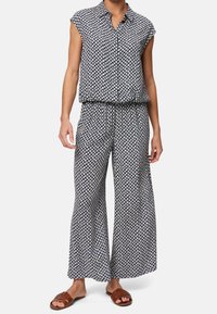 Top senza maniche con bottoni, caratterizzato da un motivo a diamante blu navy e bianco; pantaloni abbinati a campana; tessuto leggero; modello con sandali marroni.
