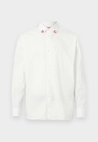 Cămașă albă cu buton, din bumbac, cu un guler clasic. Prezintă accente roșii pe vârfurile gulerului și un design simplu. Textură uniformă.