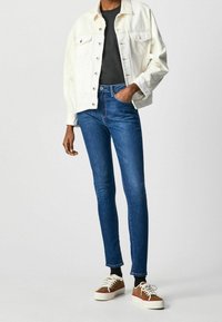 Vitt denimjacka, svart skjorta, blå smala jeans och bruna sneakers med vita sulor. Har metalldetaljer och en avslappnad passform för jackan.