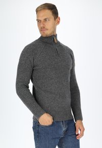 Maglione grigio a coste con colletto alto e mezza zip, caratterizzato da maniche lunghe e un motivo a maglia testurizzato. Indossato con jeans blu.