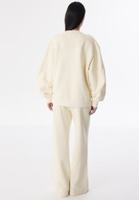 Světle krémová oversized mikina s embosovanými květinovými vzory, doplněná o široké kalhoty ve stejném stylu. Měkká látka, volný střih, minimální švy.