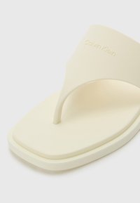 Calvin Klein flip-flop in light cream, featuring a flat, square toe, textured strap, and embossed logo on the upper.