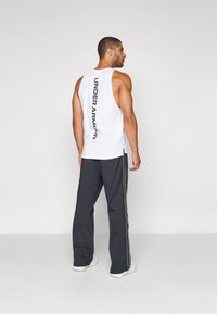 Balts bez piedurknēm T krekls ar uzrakstu "UNDER ARMOUR" vertikāli aizmugurē. Kombinēts ar tumši pelēkiem sporta biksēm, kuru malās ir baltas svītras.