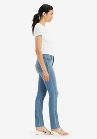 Jeans ajustados de color azul con cintura media, con bolsillos traseros con costuras en forma de corazón, combinados con una camiseta blanca ajustada y zapatillas blancas.