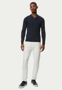 Námořnický pletený svetr s véčkovým výstřihem, nošený s bílými slim-fit džínami a černými teniskami. Tento outfit má slim fit design a minimální akcenty.