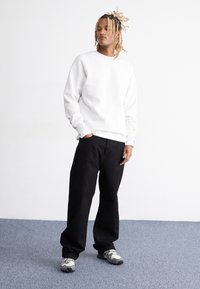 Hvid crewneck sweatshirt parret med løse sorte bukser og grå sneakers. Glat stof uden synlige mønstre, afslappet pasform.