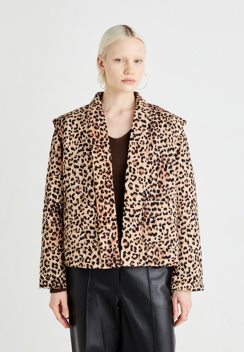 Leopardprint jakke med myk tekstur, dristig mønster og strukturert krage. Kombinert med en brun topp og sorte skinnbukser.
