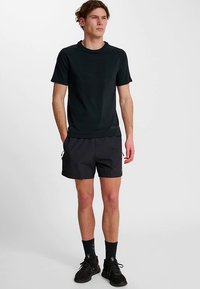 Svart t-shirt med kort ärm i bomull, kombinerad med svarta sportshorts med sidofickor och dragsko. Svarta skor kompletterar outfiten.