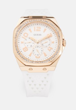 Montre en silicone blanc avec un boîtier octogonal en or rose, accents en cristal, un cadran blanc, de gros chiffres et trois sous-cadrans pour le jour et l'heure.