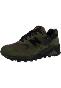 Zapatilla de ante verde y malla con acentos negros, que presenta una suela texturizada y un cuello acolchado, diseñada para comodidad y tracción.
