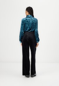 Turquoise velvet shirt with a collar, paired with high-waisted black wide-leg pants. Smooth texture and casual fit.