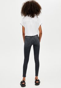 Jeans skinny negros de cintura alta, con cinco bolsillos y un diseño limpio, combinados con una blusa blanca de corte holgado y sandalias negras.
