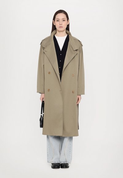 Khaki trench coat with double-breasted buttons and shoulder epaulets, layered over a black cardigan and light blue wide-leg jeans.