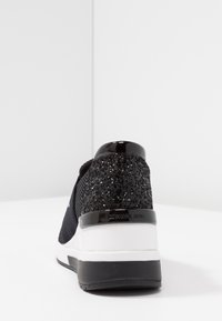 Sneaker nera con tacco testurizzato e luccicante. Parte superiore in tessuto nero liscio, suola intermedia bianca e suola esterna nera in gomma. Marchio sottile sul tacco.