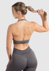 Grijze sportieve crop top en hoge taille leggings, met ribbelstructuur en logo-accenten. Diepe uitsnede op de achterkant van de top.