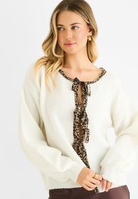 Pullover lavorato a maglia color crema con scollatura a barchetta, dotato di un nastro a pois leopardato annodato nella parte anteriore e maniche lunghe e ampie.