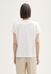 Weißes Baumwoll-T-Shirt mit kurzen Ärmeln und lockerer Passform, mit Rundhalsausschnitt und roten Akzenten an den Schultern, von hinten betrachtet.