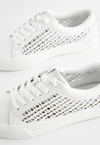 Sneakers bianchi con design perforato sui lati, lacci piatti, suola in gomma testurizzata e materiale in pelle liscia. Forma semplice e moderna.