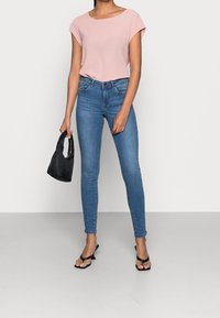 Camisetta rosa chiaro a maniche corte, jeans blu slim-fit, borsa nera a mano e sandali neri con cinturini. Design semplice e texture liscia.